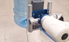 Cobot de 6 ejes con ventosa de vacío levantando un garrafón de agua sobre una tarima